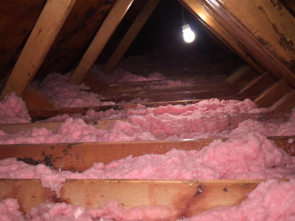 Wet fiberglass insulation between attic joists with water stains
